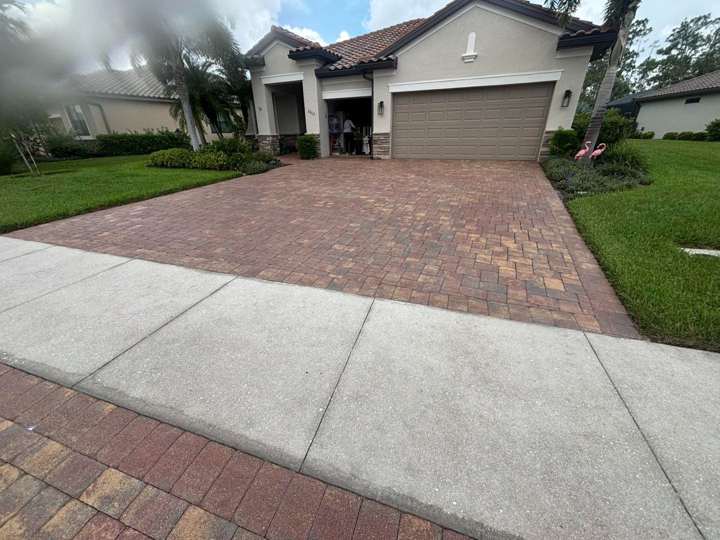 Brown paver driveway leading to a double garage with landscaped lawn