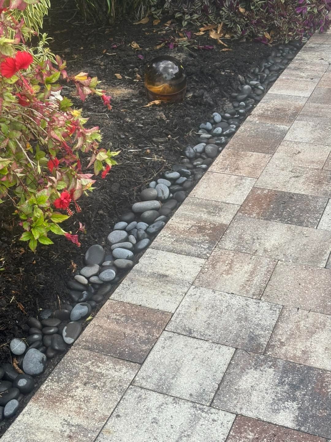 Close view of multicolored paver edging beside dark mulch and flowering shrubs