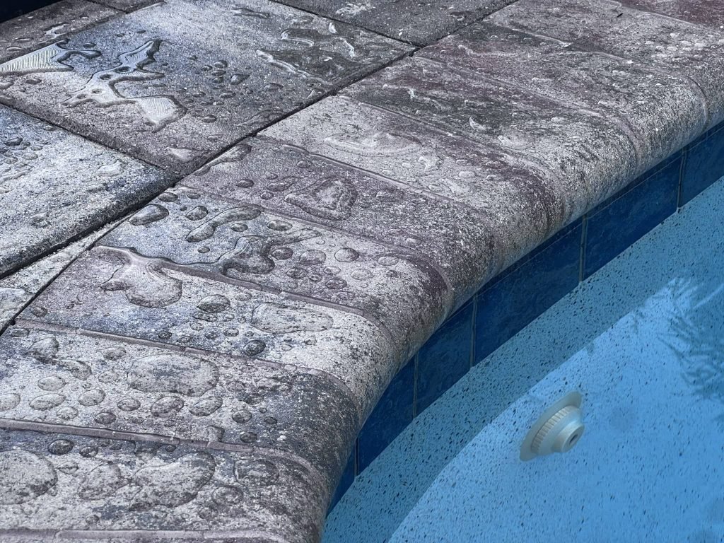 Close view of textured gray pool coping above blue waterline tiles