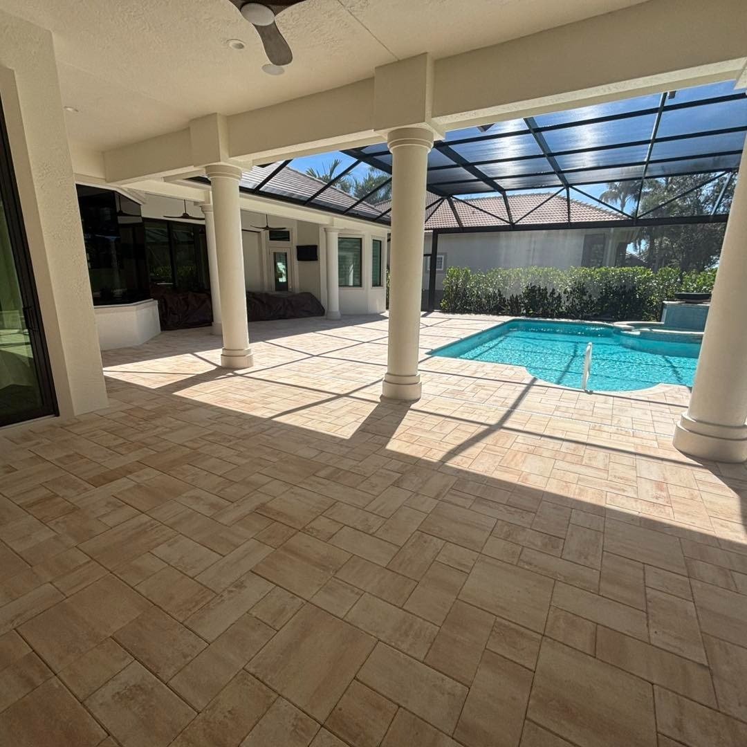 Covered patio with beige pavers and white columns beside a screened swimming pool