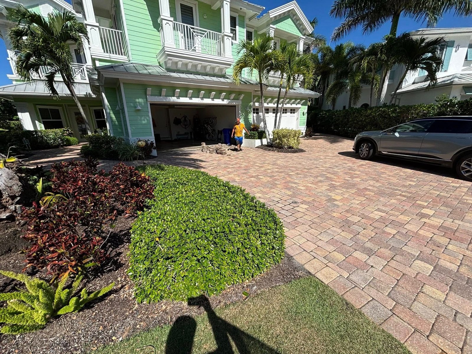 Curved multicolored paver driveway outside a green house with balconies