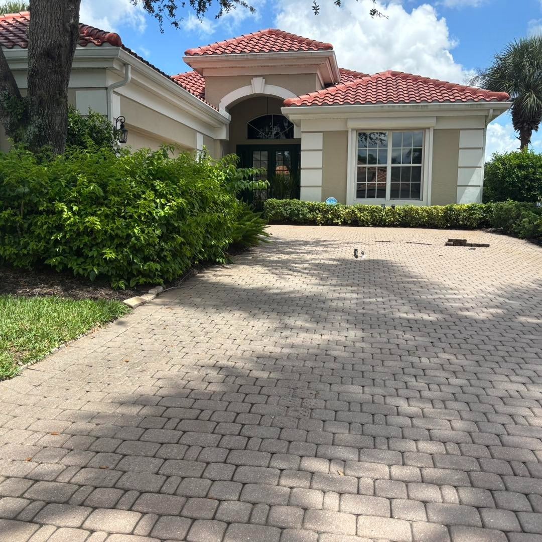 Curved small-block paver driveway approaching a house with a red tile roof