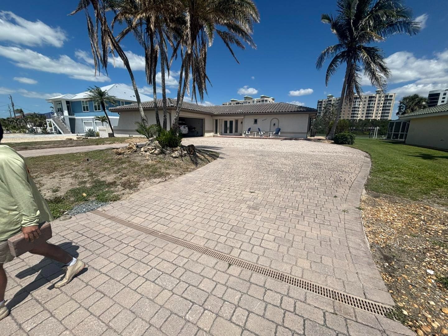 Curving gray paver driveway beside palm trees approaching a single-story home