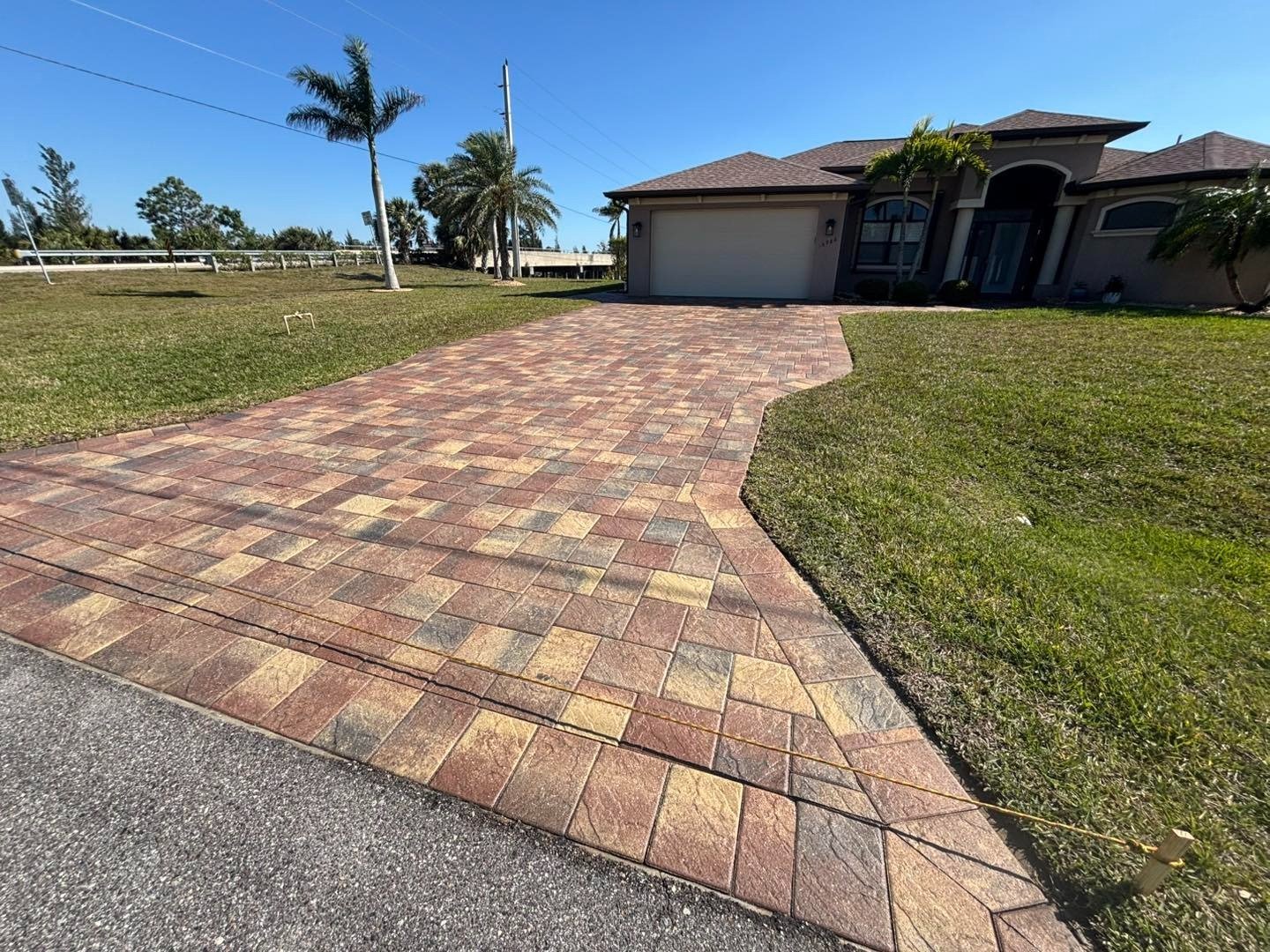 Curving multicolored paver driveway leading to a house with open lawn