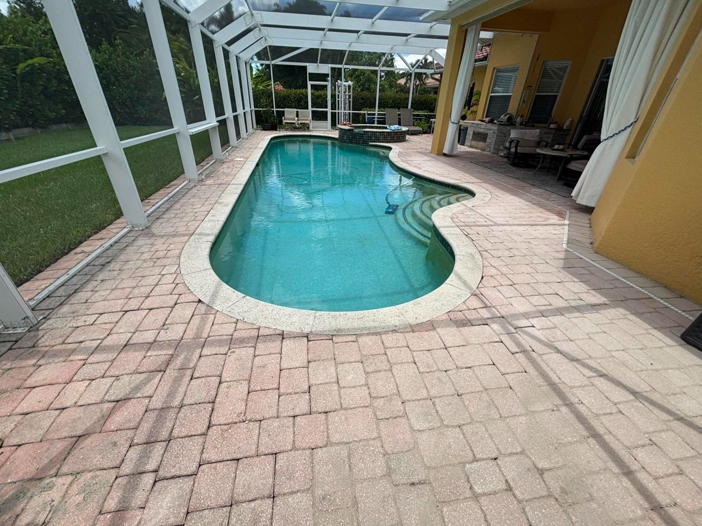 Curving screened swimming pool surrounded by a reddish rectangular paver deck