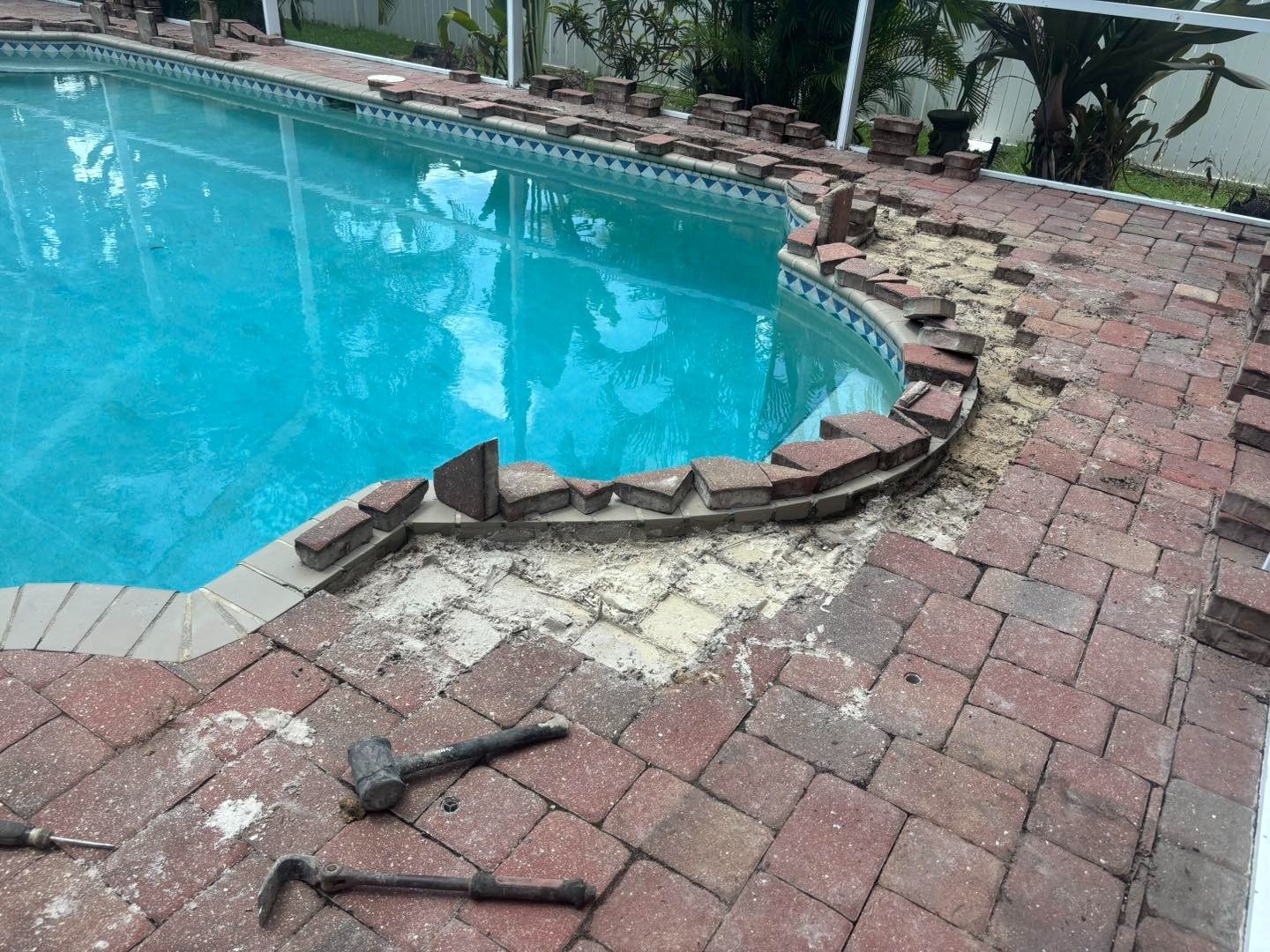 Displaced pool coping and loose reddish pavers around a curved swimming pool edge