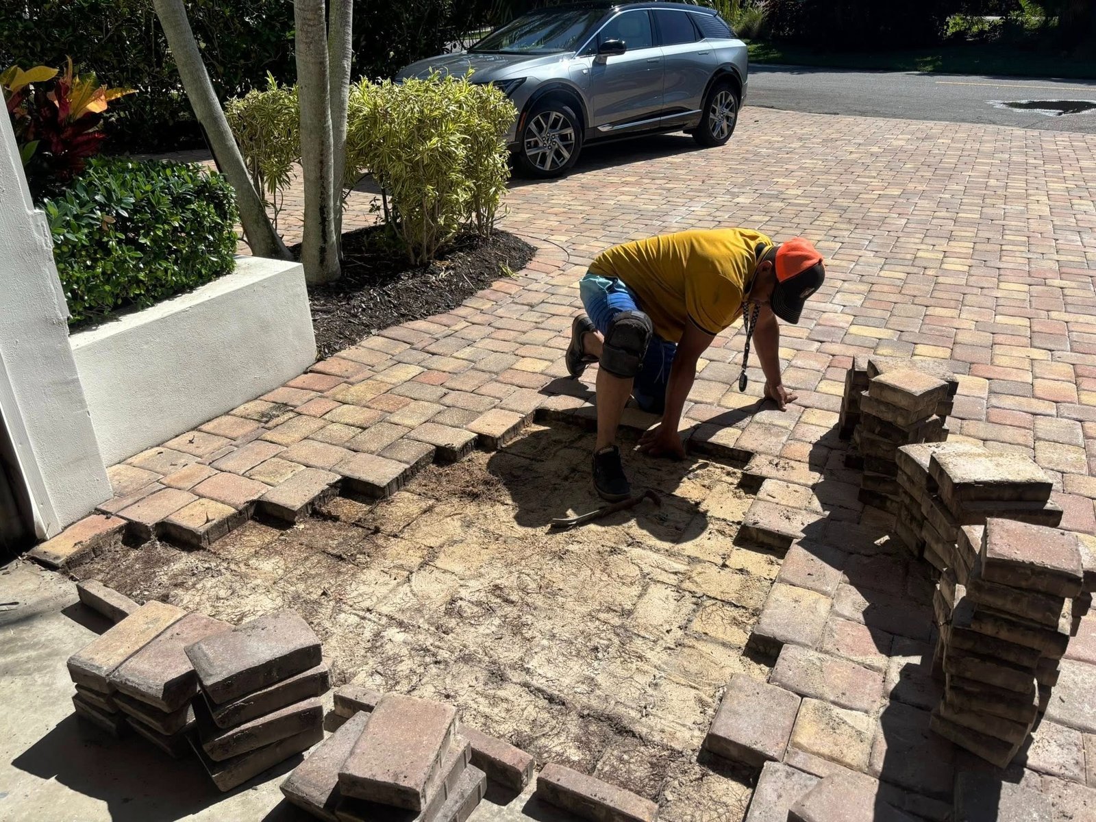 Worker removing pavers from a driveway with exposed ground and nearby stacks