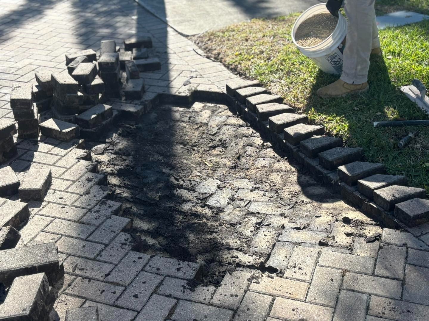 Driveway section with pavers removed and stacked around exposed base