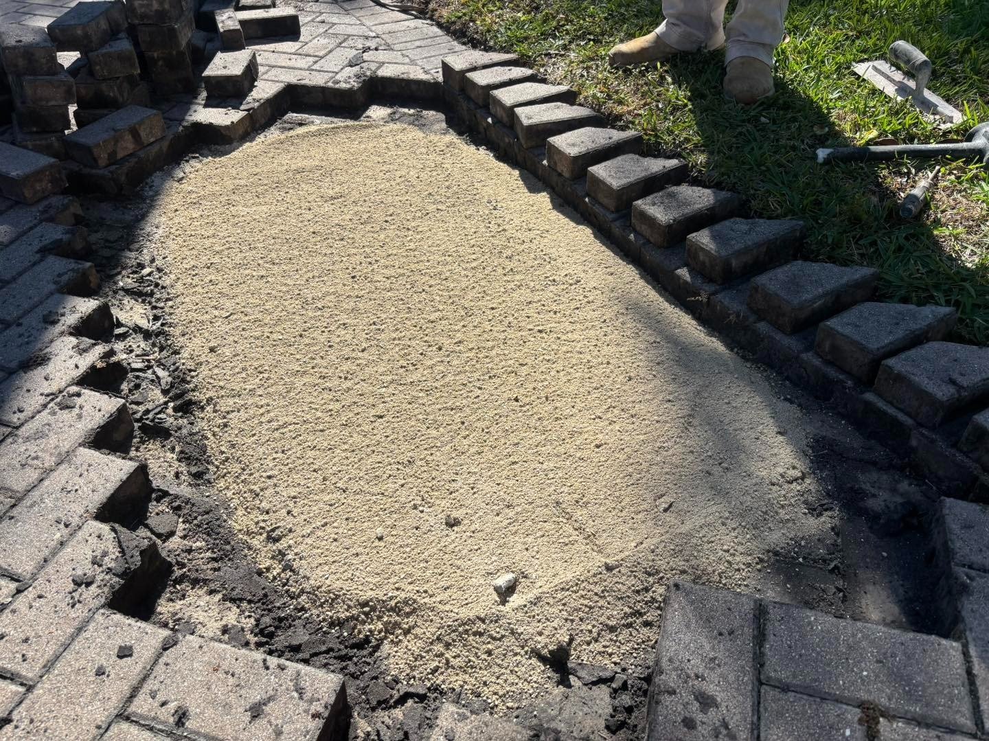 Exposed driveway base filled with pale sand between stacked pavers