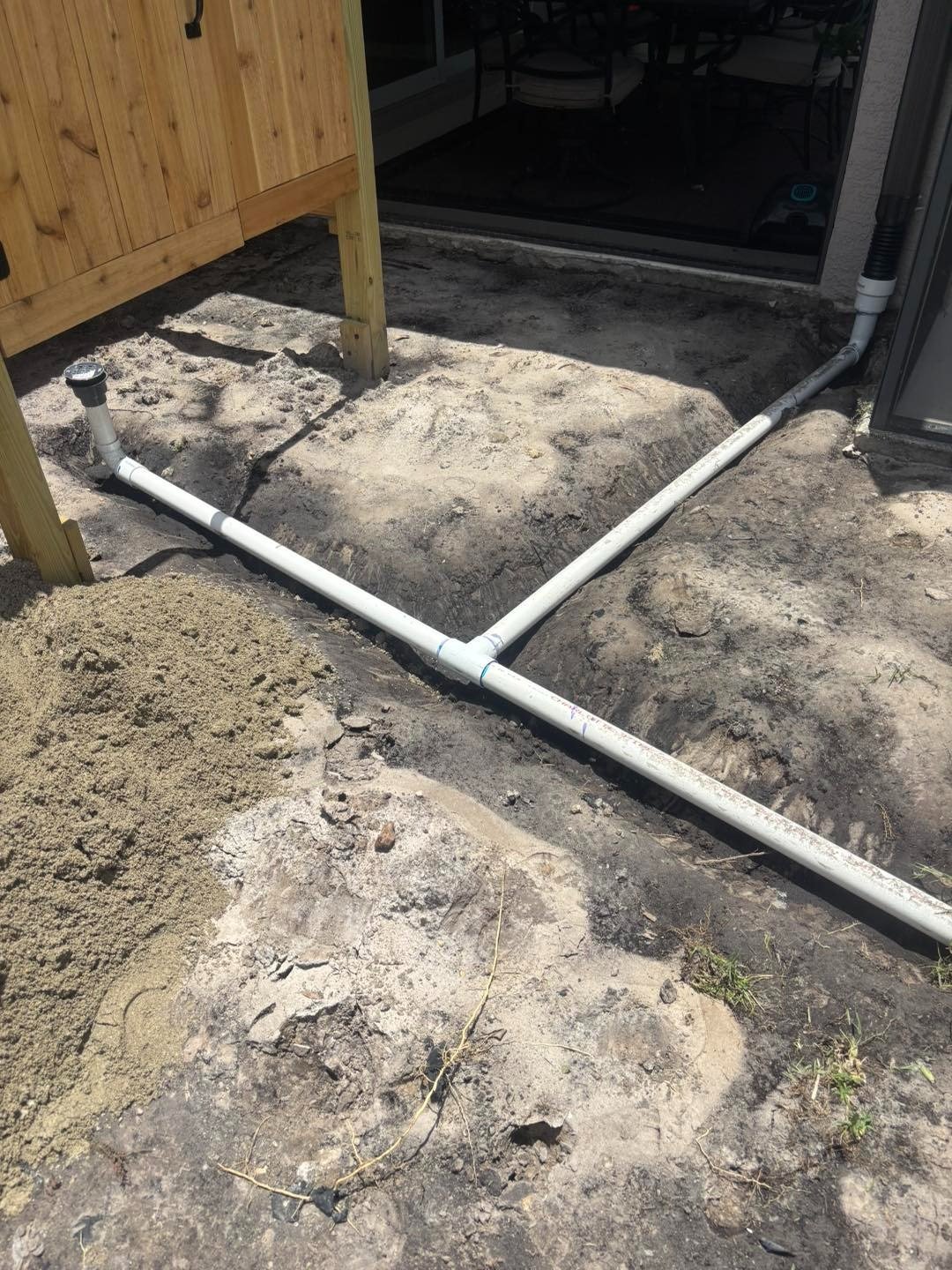 Exposed ground and white pipe beneath a wooden outdoor shower enclosure