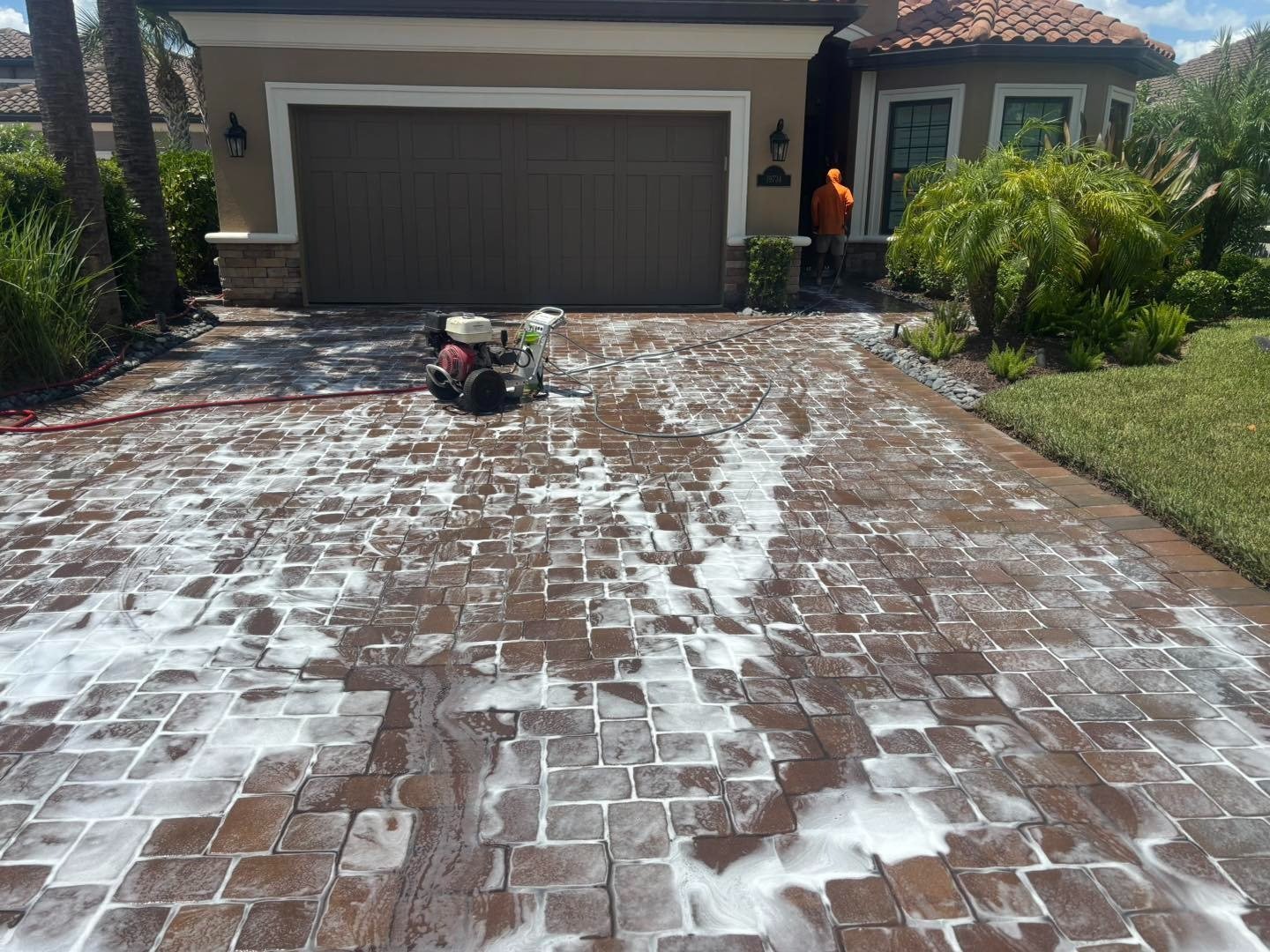 Foamy paver driveway with washing equipment outside a dark double garage