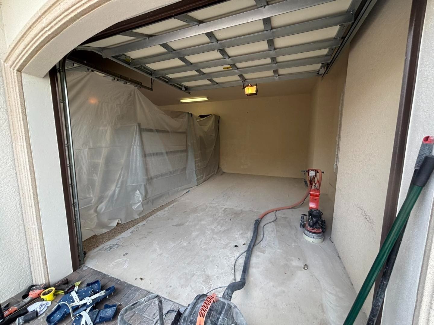 Garage floor preparation with grinder, hose, and protective wall covering