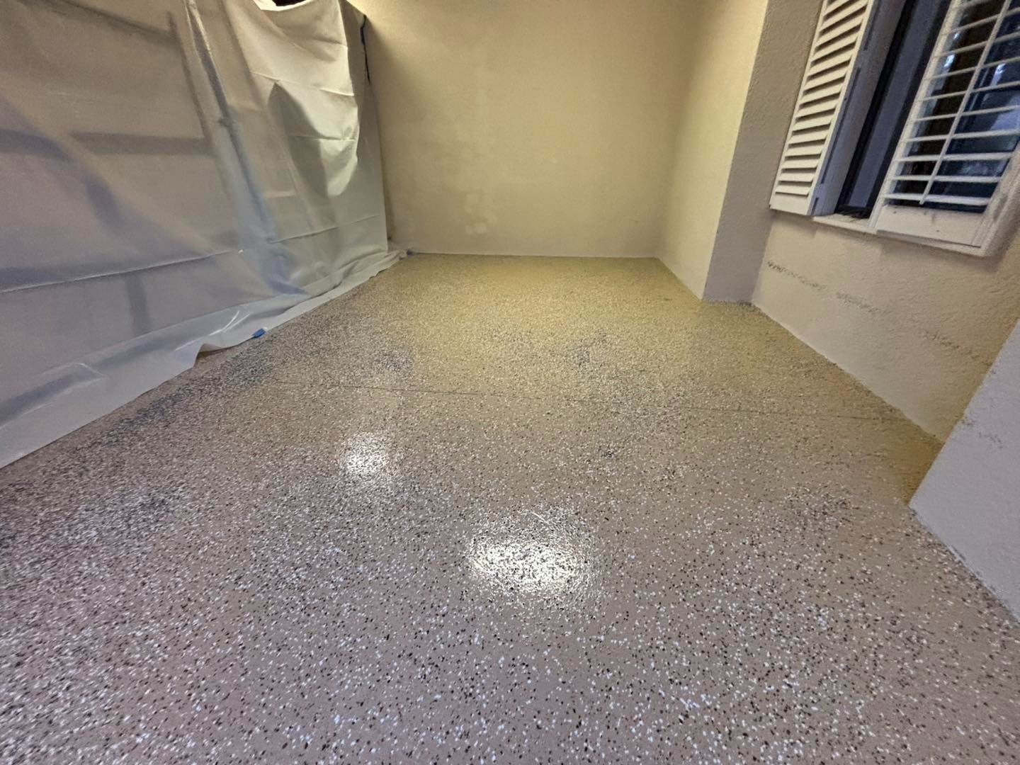 Glossy speckled garage floor beside protective plastic and shuttered window