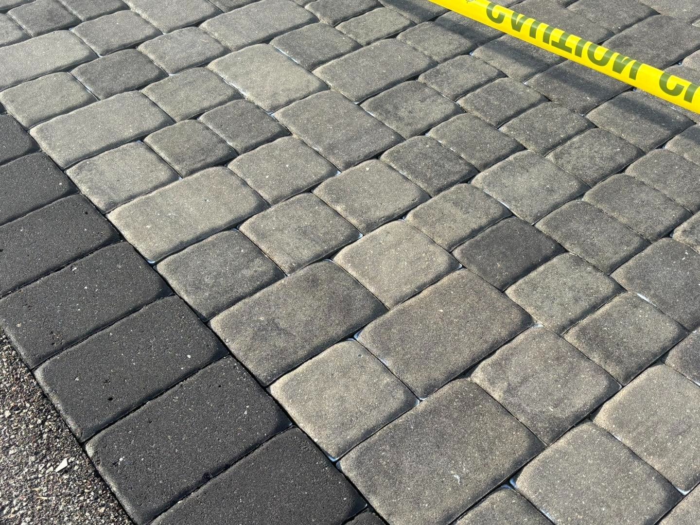 Gray driveway pavers and dark border beneath yellow caution tape
