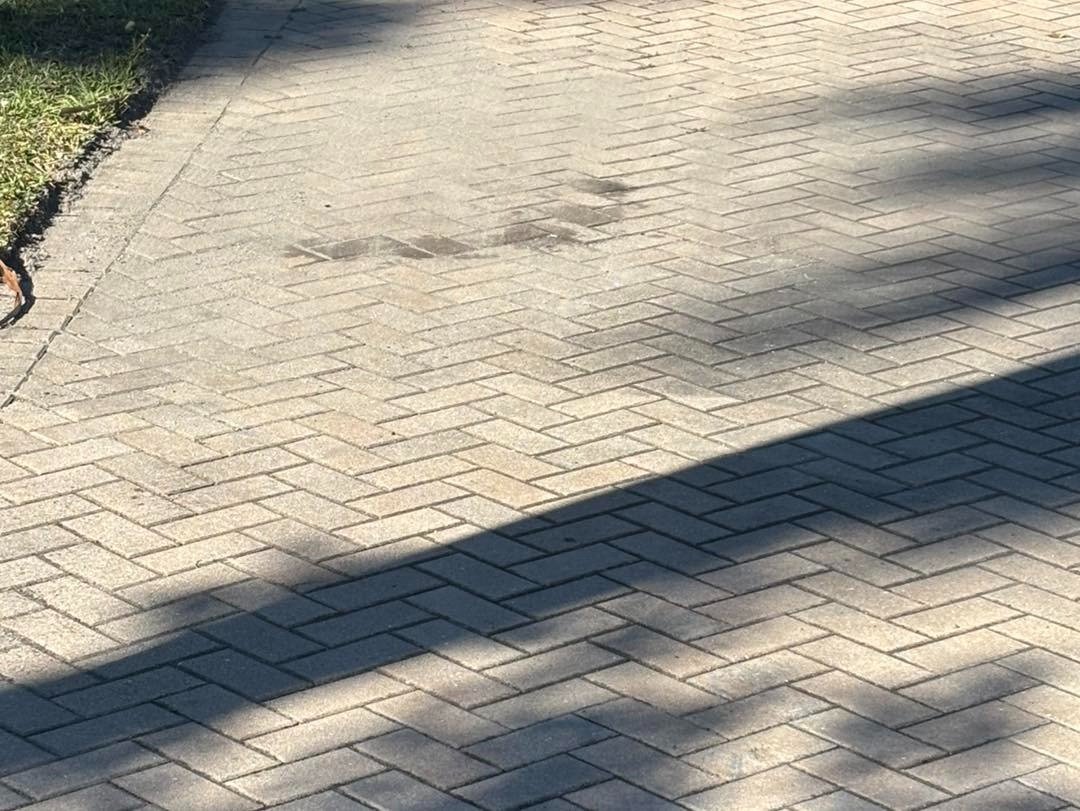 Gray herringbone driveway pavers crossed by shadows from nearby trees