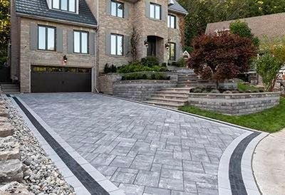 Gray paver driveway with dark curved borders outside a large brick house