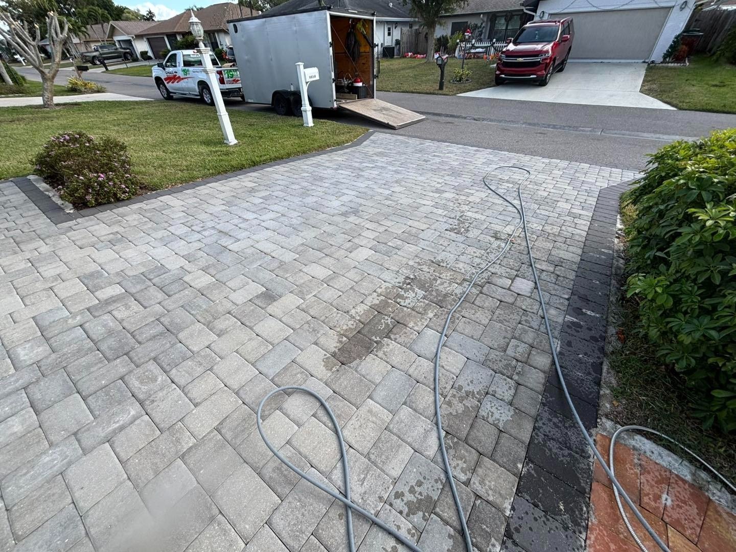 Gray paver driveway with hose beside a trailer at the street