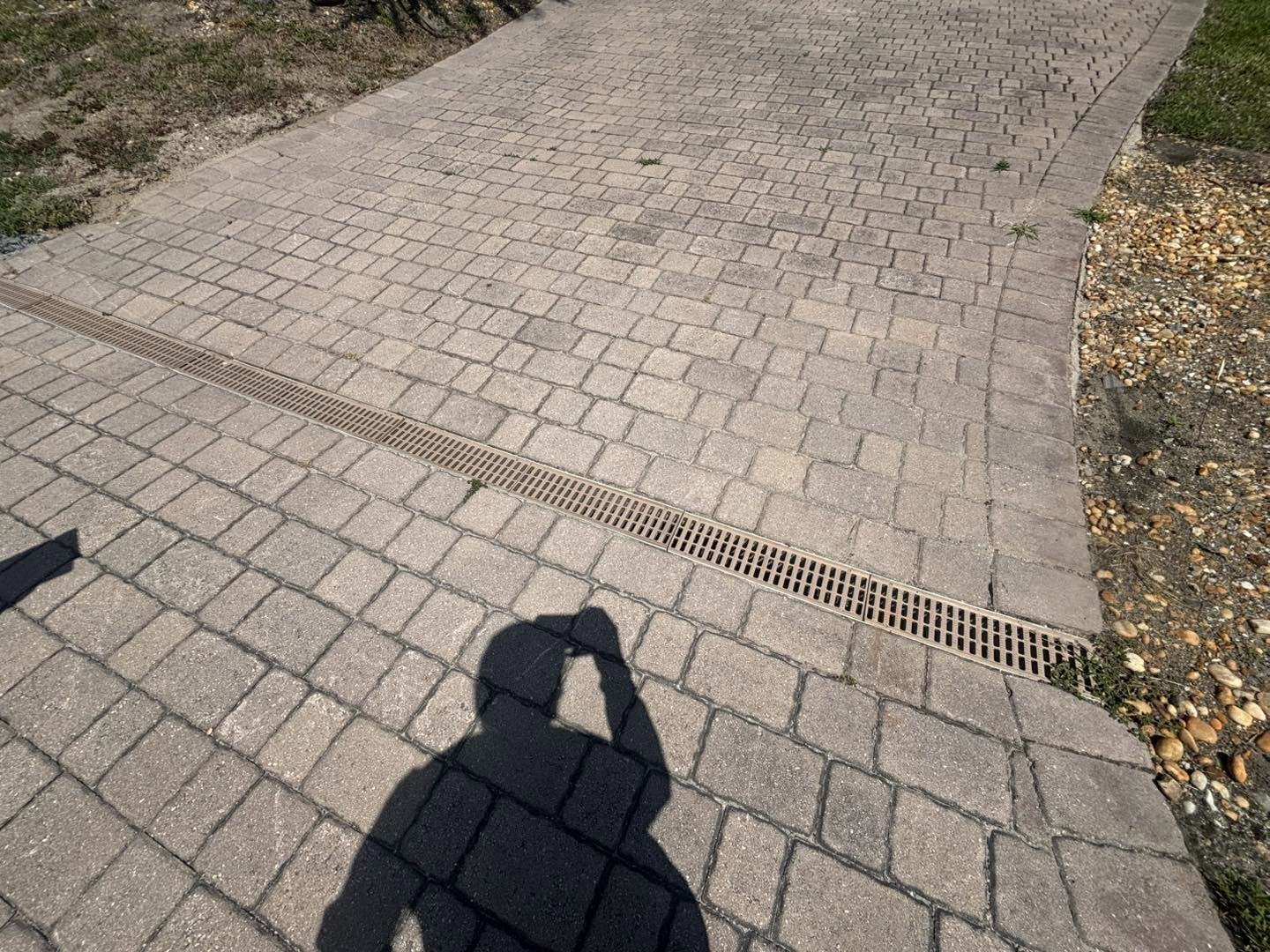 Gray paver driveway with a drainage channel and shadow across the foreground
