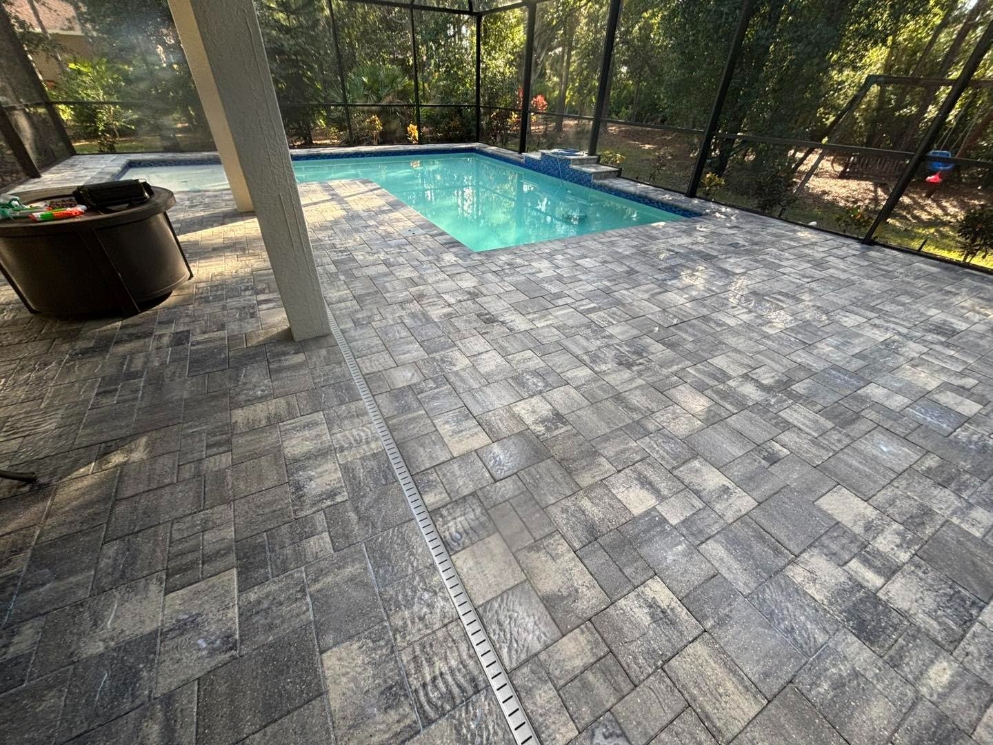 Gray paver pool deck inside a screened enclosure with wooded backdrop