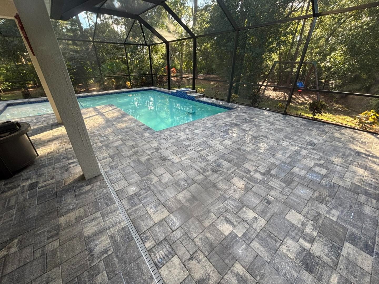 Gray rectangular pavers surrounding a swimming pool inside a screened enclosure