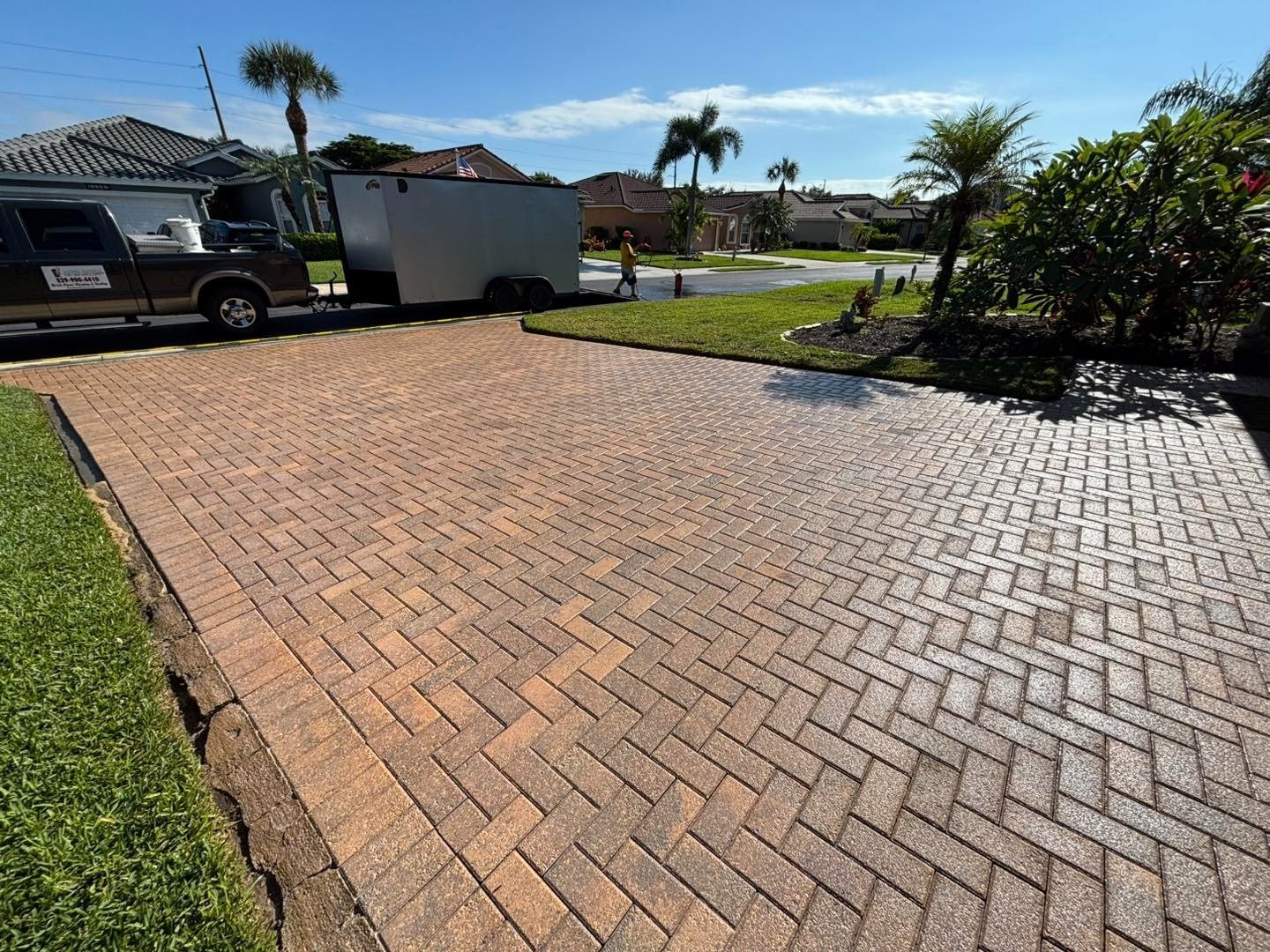 Wide herringbone paver driveway with work vehicles parked near the street