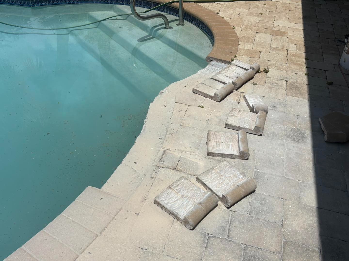Lifted pale pavers beside a curved pool edge and metal handrail