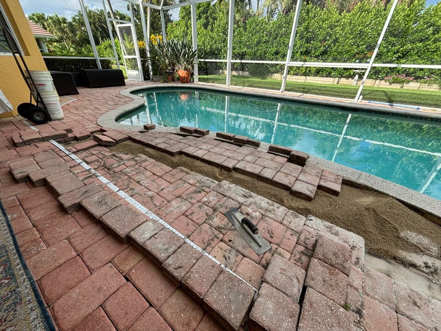 Lifted reddish pavers and exposed ground along the edge of a swimming pool