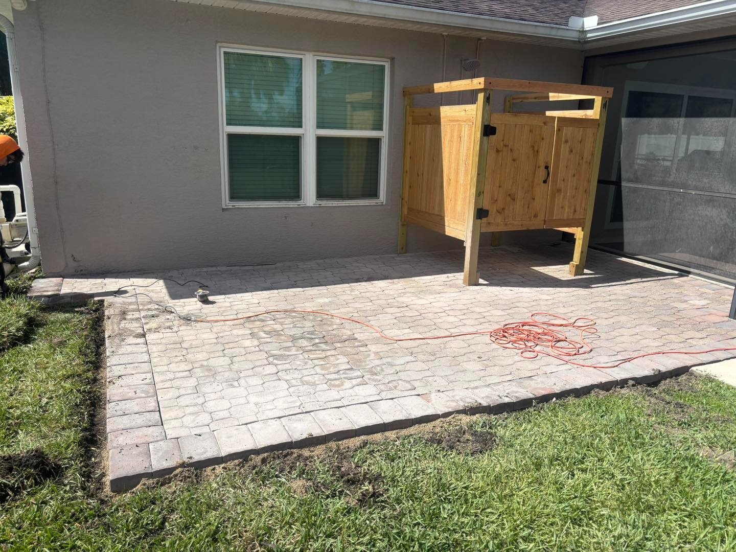 Light paver patio beside a wooden outdoor shower and screened pool enclosure