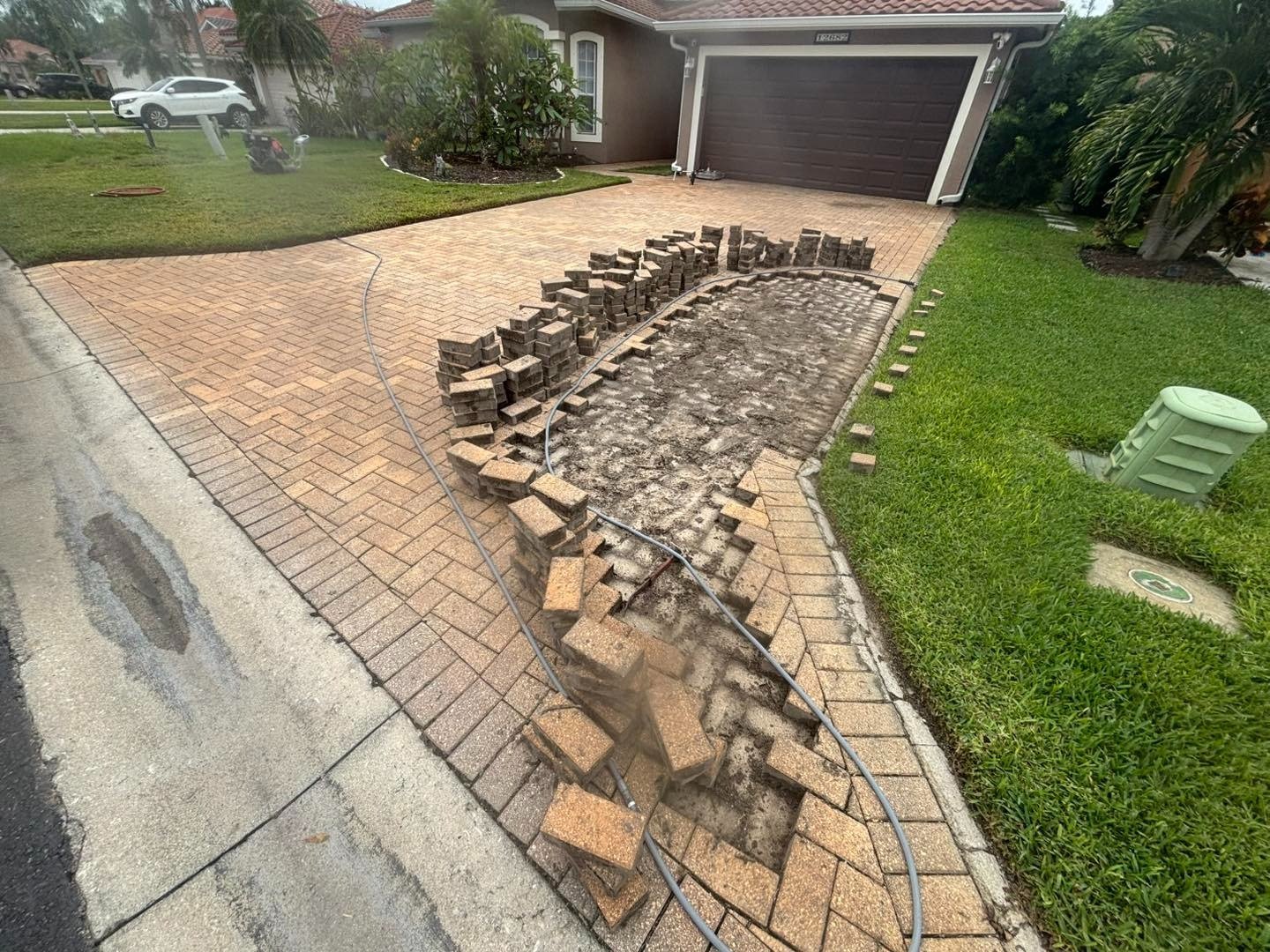 Long driveway section with removed pavers stacked along exposed base