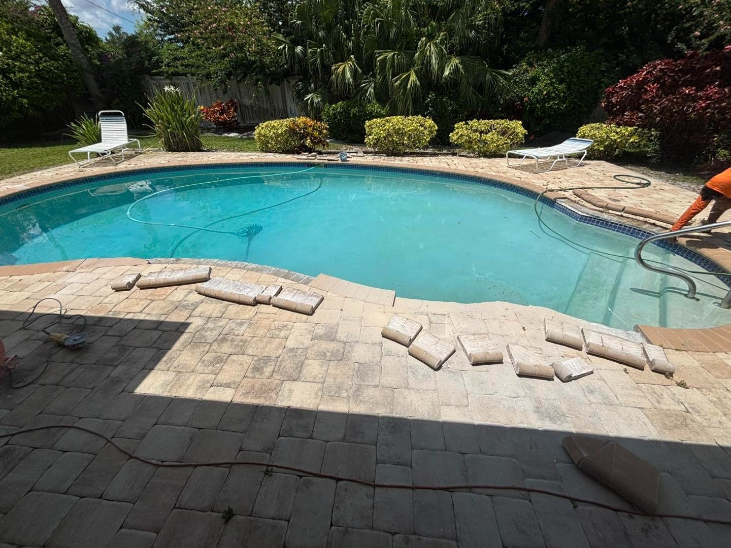 Loose pale pavers arranged along the curved edge of a swimming pool