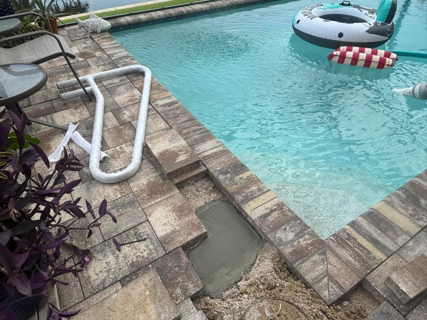 Loose pavers and exposed base beside a pool ladder and floating toys