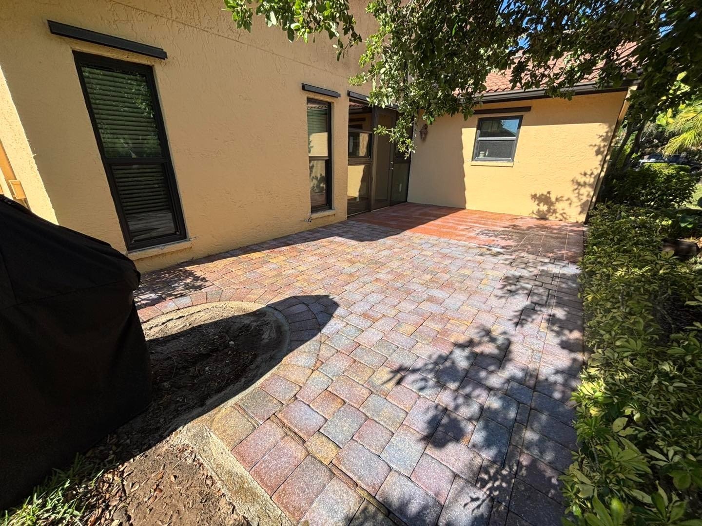 Multicolored paver courtyard beside a yellow house and planted borders