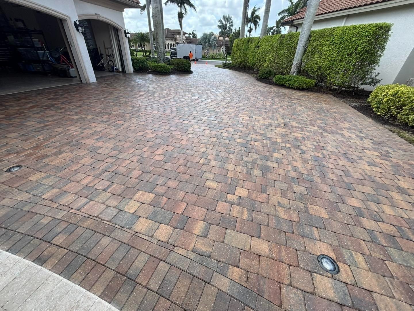 Multicolored paver driveway beside an open garage and tall hedge