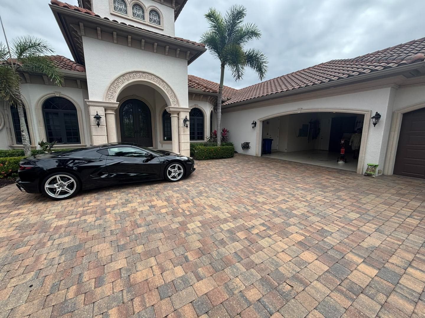 Multicolored paver driveway outside a two-story house with a black convertible