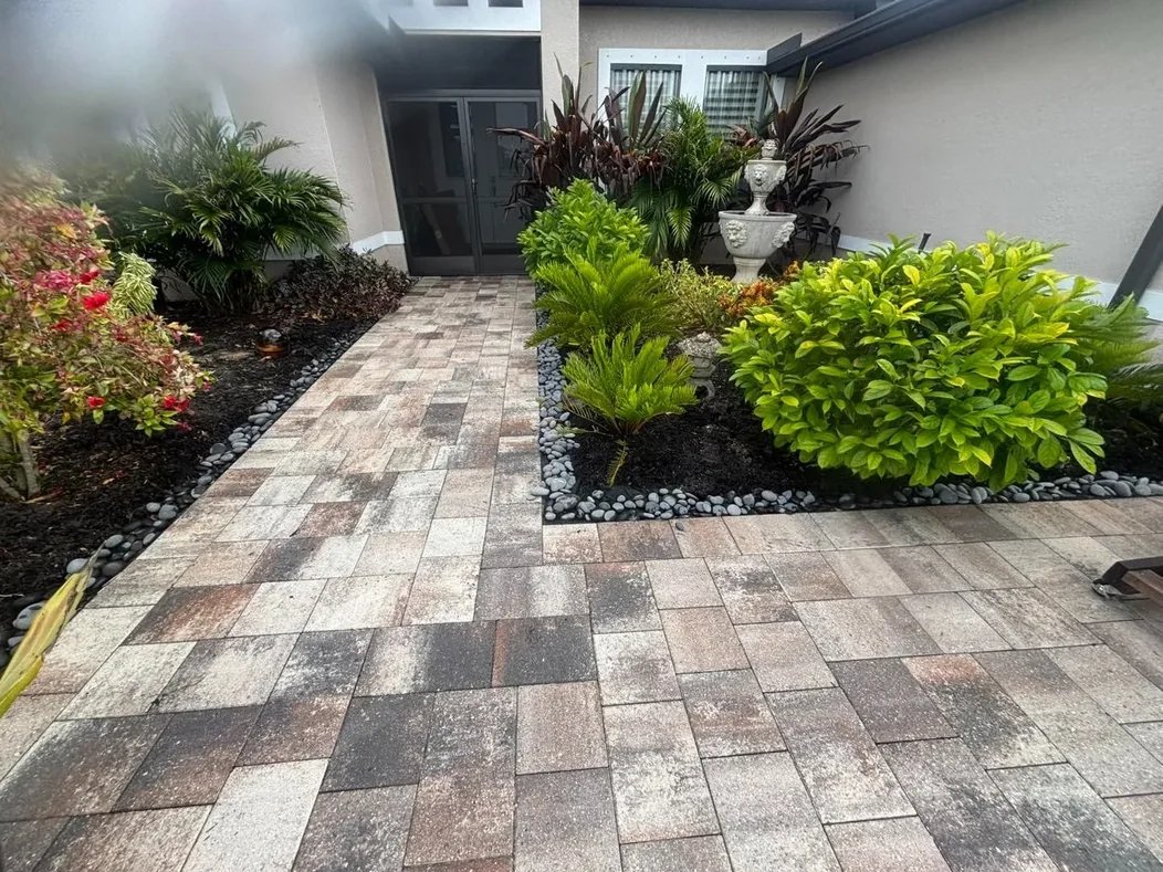 Multicolored paver entry walkway between planted beds leading to a front door
