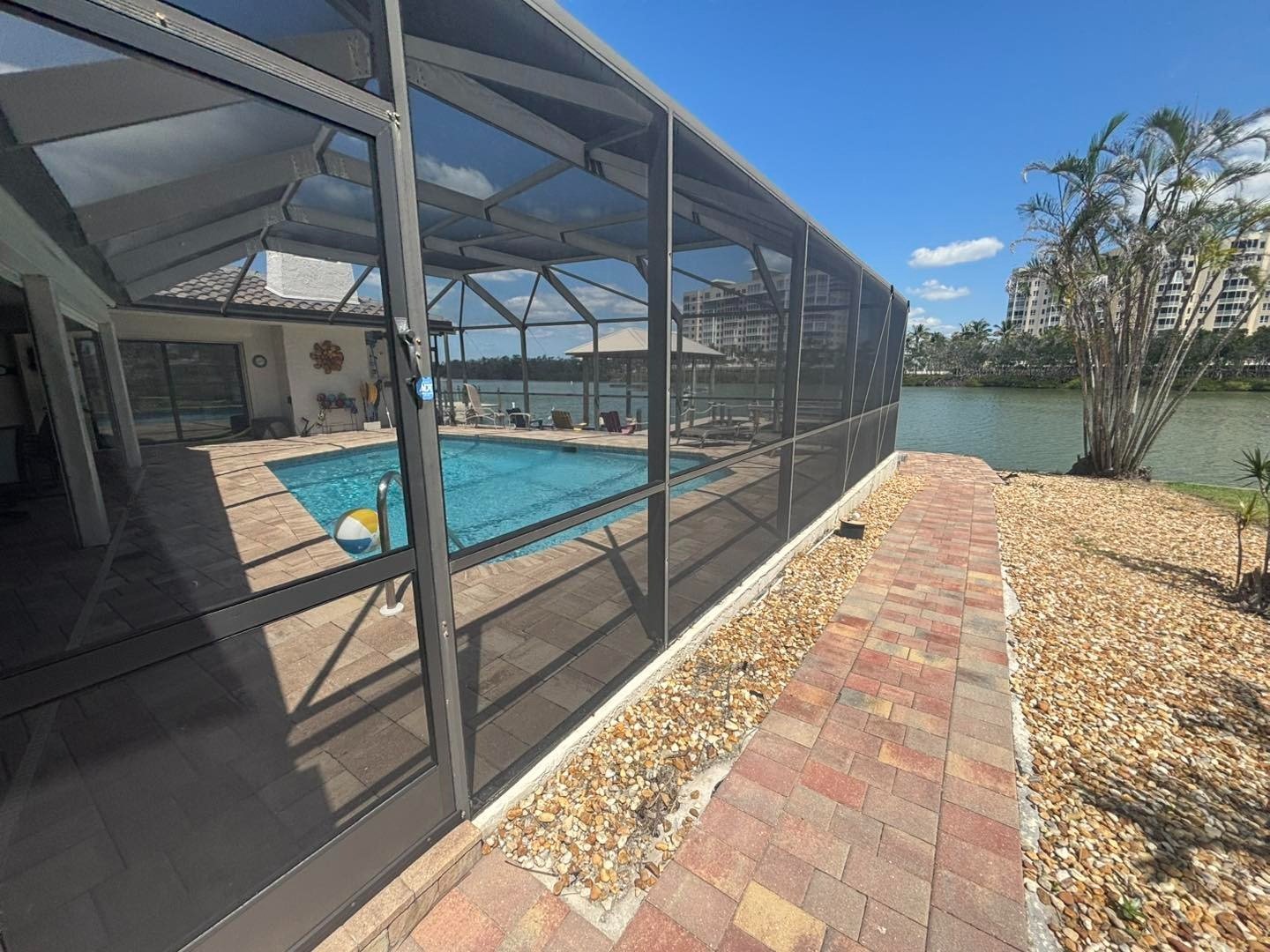 Narrow red paver walkway beside a screened pool enclosure and gravel bed