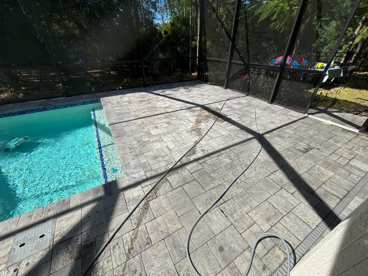 Large pale deck tiles beside a screened swimming pool with dark enclosure shadows
