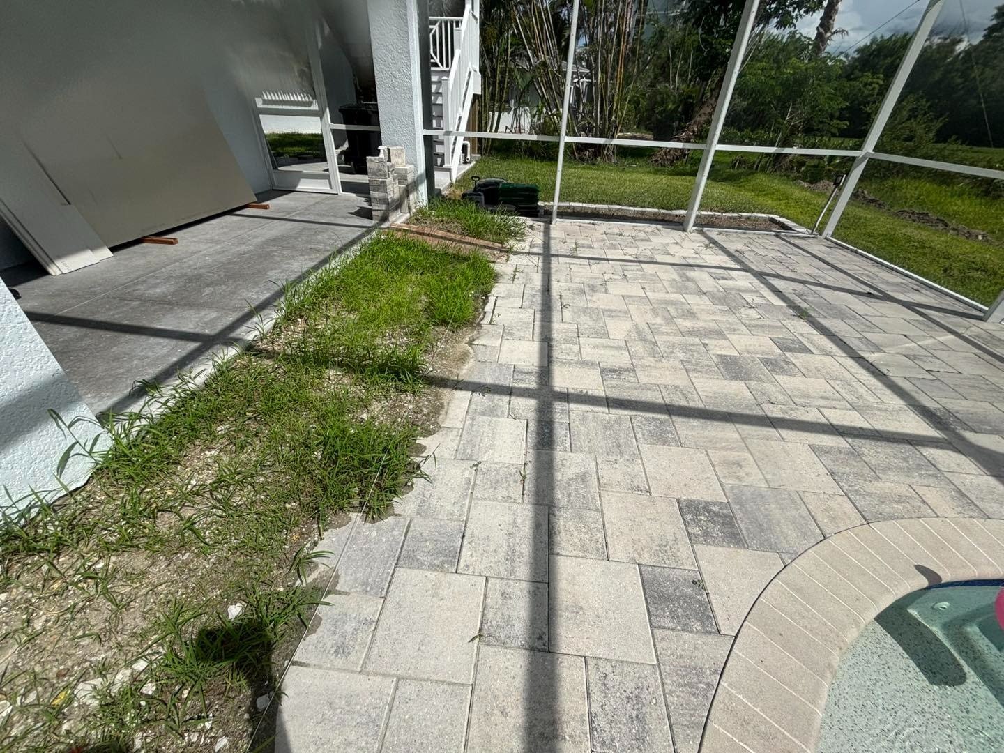 Pale rectangular pool deck pavers beside a strip of grass inside a screen enclosure