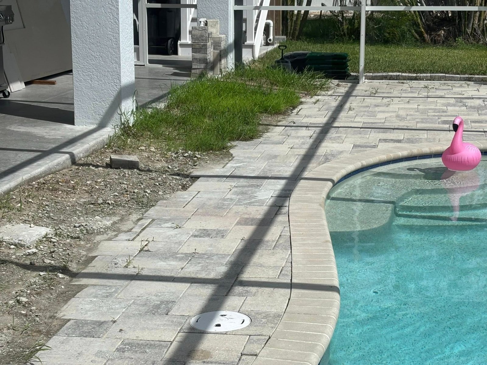 Partially removed pool deck with exposed base beside a screened swimming pool