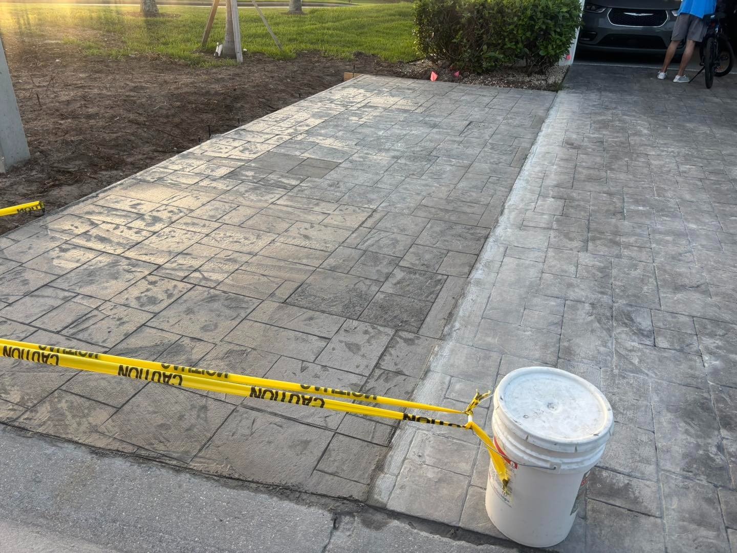 Patterned driveway with caution tape across the entrance and a white bucket