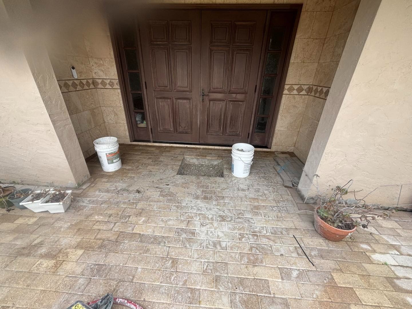 Paver front entry beneath double wooden doors with buckets on the landing