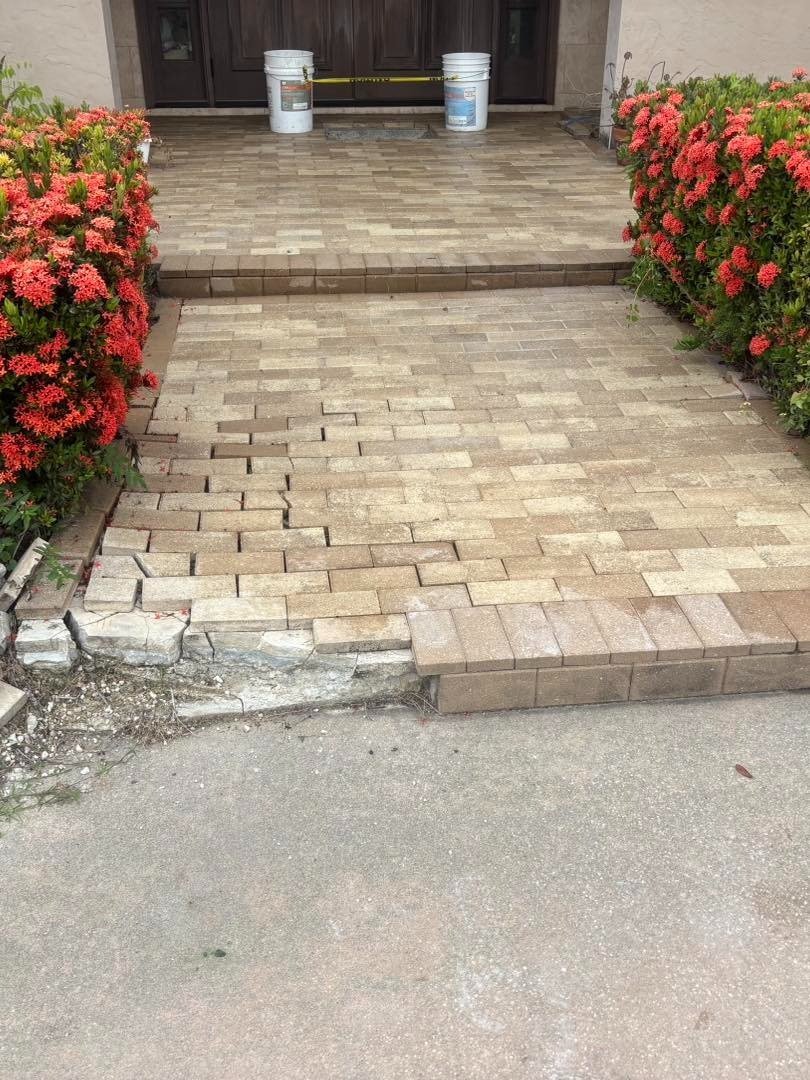 Paver front walkway with uneven blocks beside flowering shrubs and entrance steps