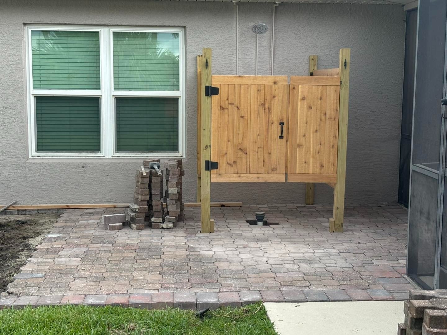 Paver patio beneath a window beside a wooden outdoor shower gate