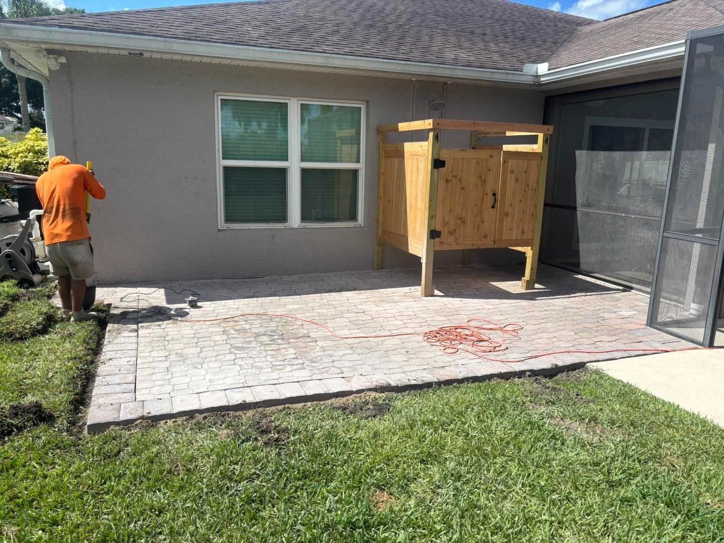 Paver patio beside a gray house with a wooden outdoor shower enclosure