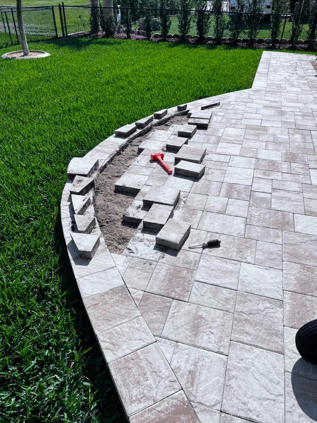 Paver patio edge with loose blocks beside a green lawn