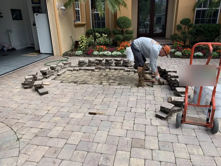 Crew member lifting driveway pavers to rebuild the sand base during a paver repair in Bonita Springs, FL