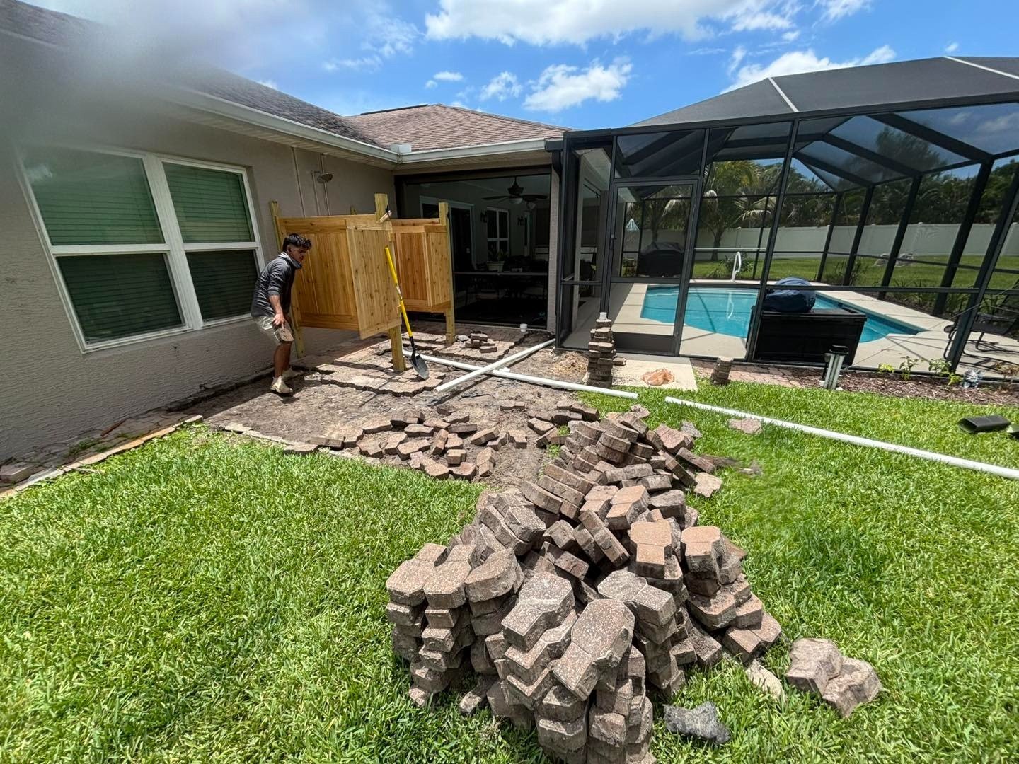 Piles of removed pavers on a lawn beside a partially opened patio