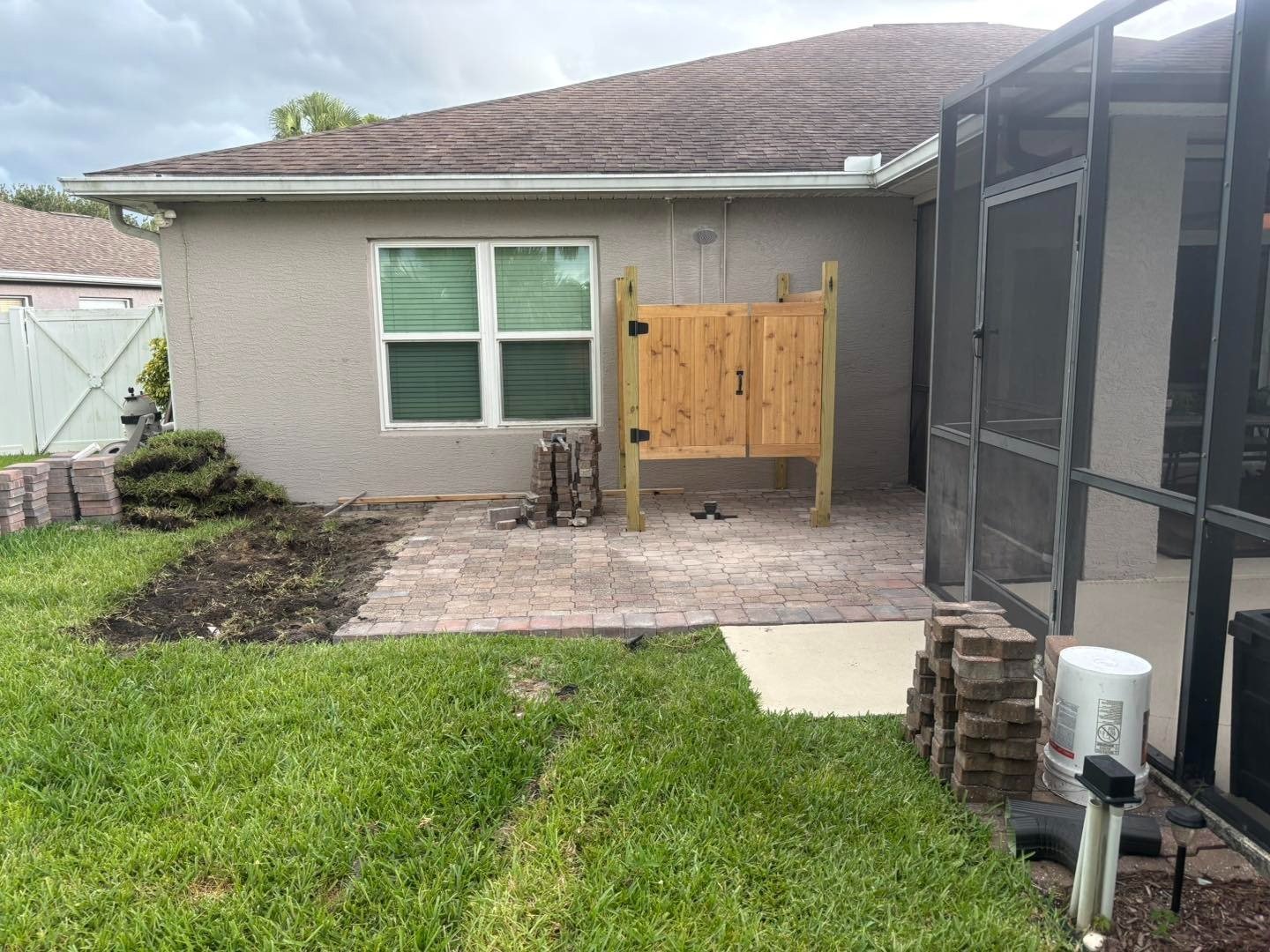 Rear paver patio beside a gray house and screened pool enclosure