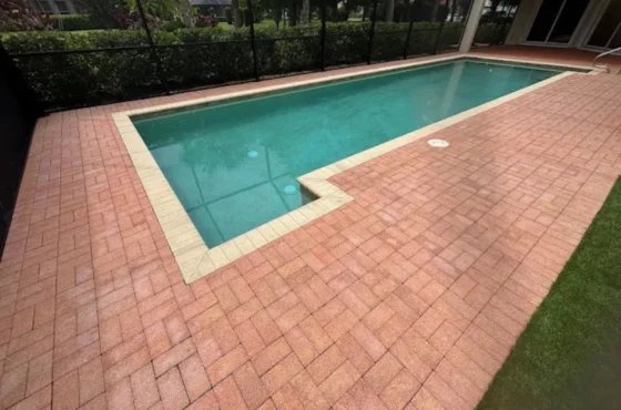 Rectangular swimming pool bordered by red pavers and pale coping