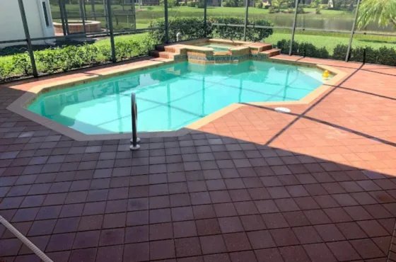 Red paver deck surrounding a screened swimming pool with raised spa